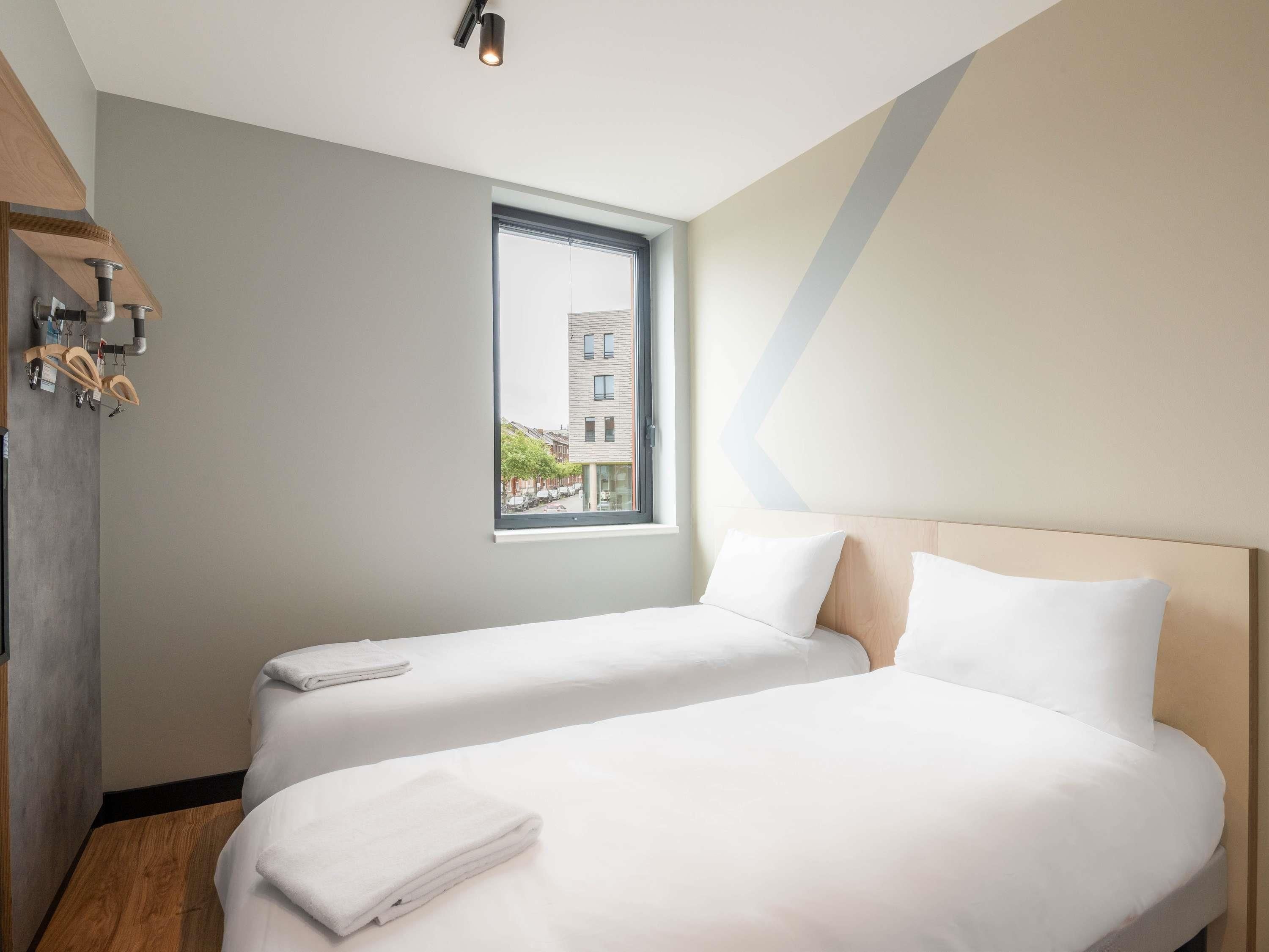 A hotel room with two beds, a window, and a view of buildings outside.