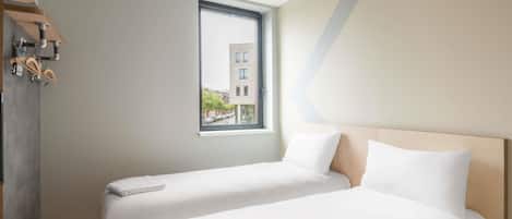 Habitación de hotel con dos camas, una ventana y vistas a edificios.