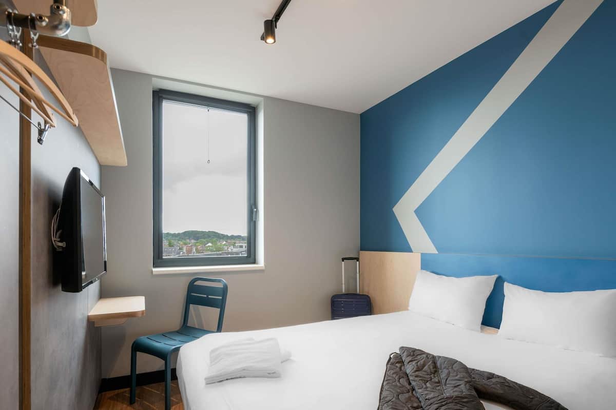 A hotel room with a bed, a desk, a chair, a TV, and a window with a view.