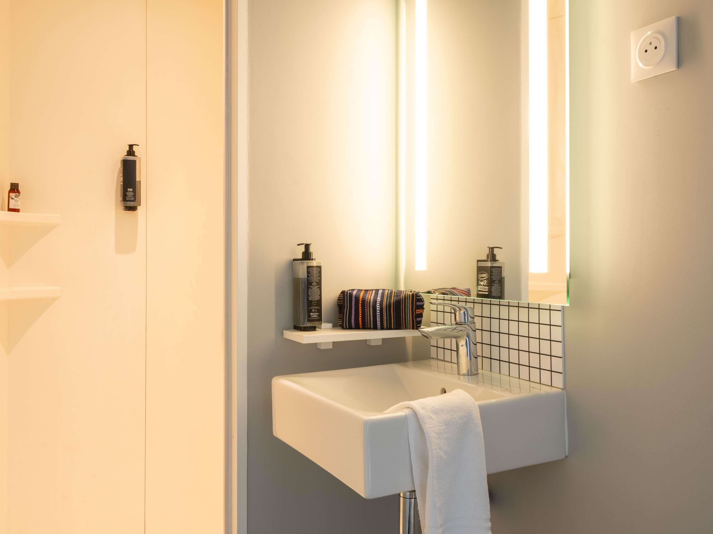 A bathroom with a white sink, a mirror, and two bottles of shampoo on a shelf.