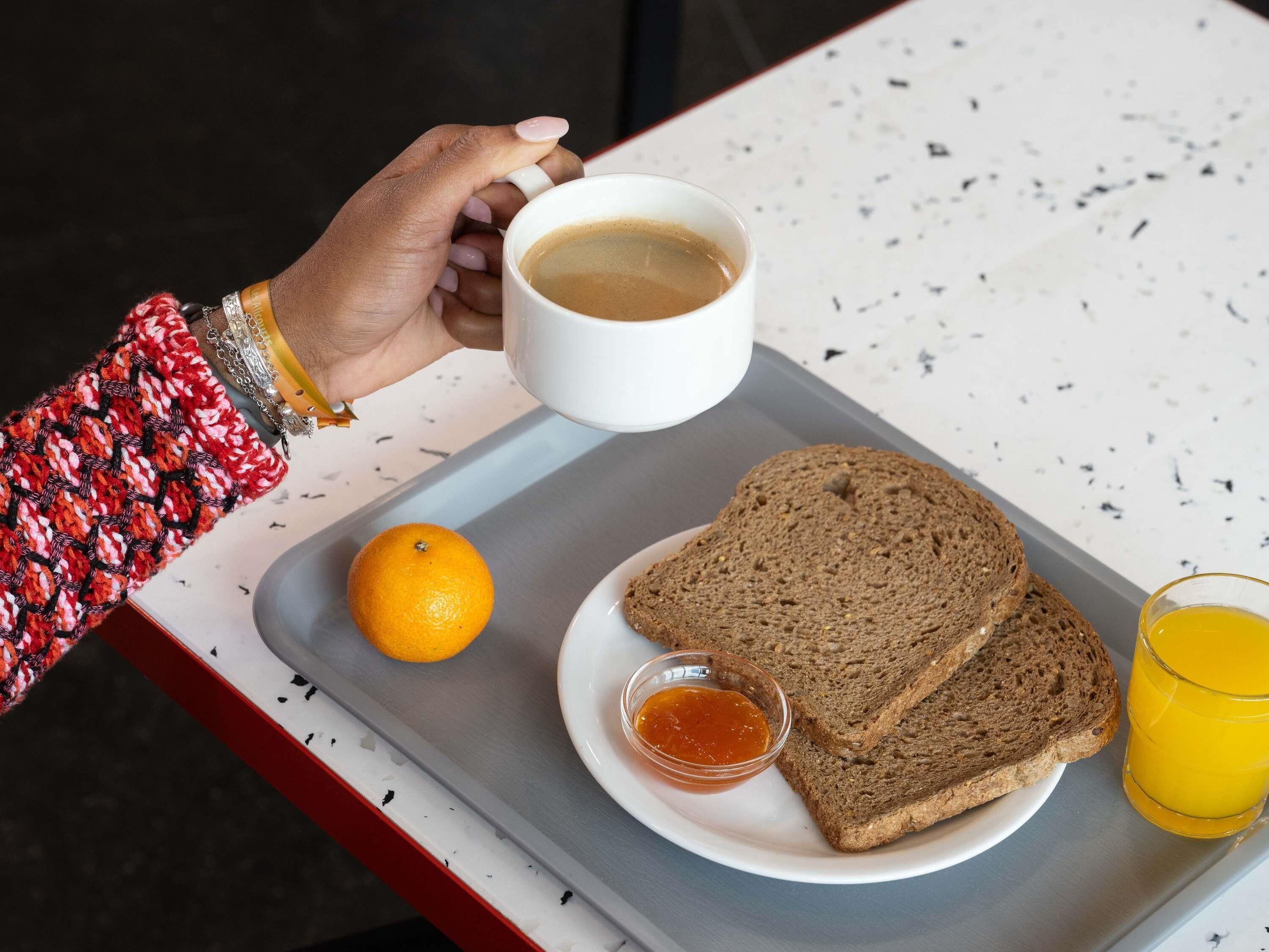 Una bandeja con dos rebanadas de pan integral, un vaso de jugo de naranja, un recipiente pequeño de mermelada y una taza de café.