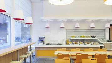 Een moderne cafetaria met hoge tafels en stoelen, een automaat en een balie met eten.