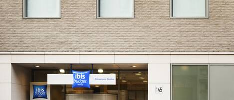 Entrada de un hotel con un cartel de ibis budget, una puerta giratoria y el número 145 en la pared.