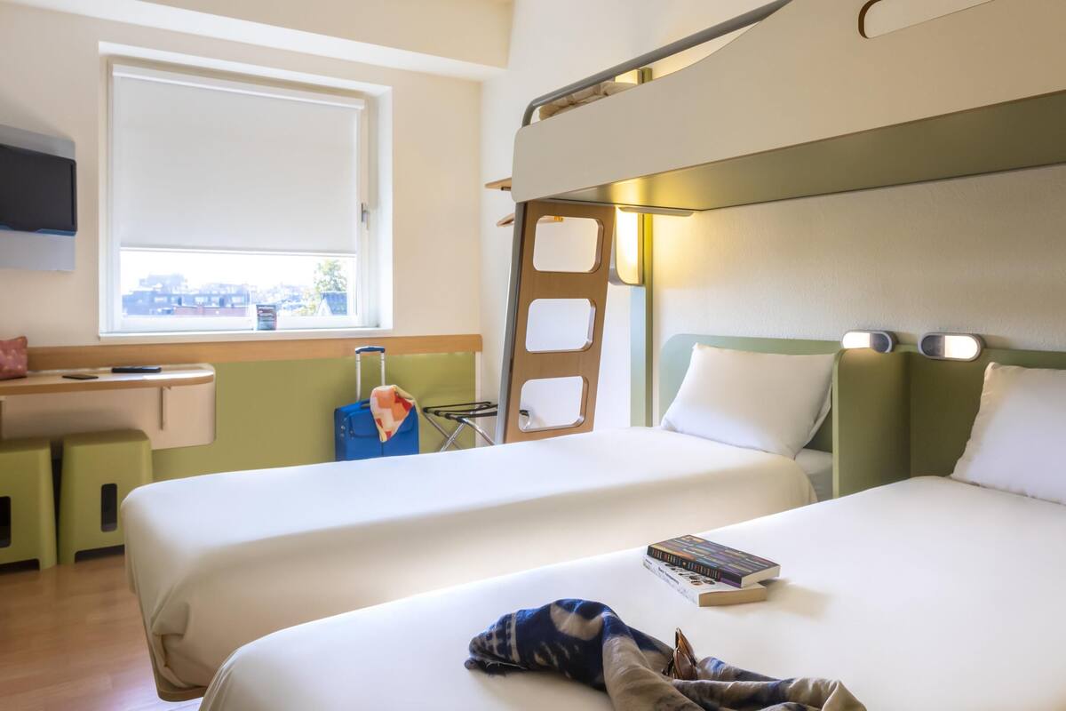 Une chambre d’hôtel avec deux lits, un bureau, une fenêtre et une vue sur les bâtiments environnants.