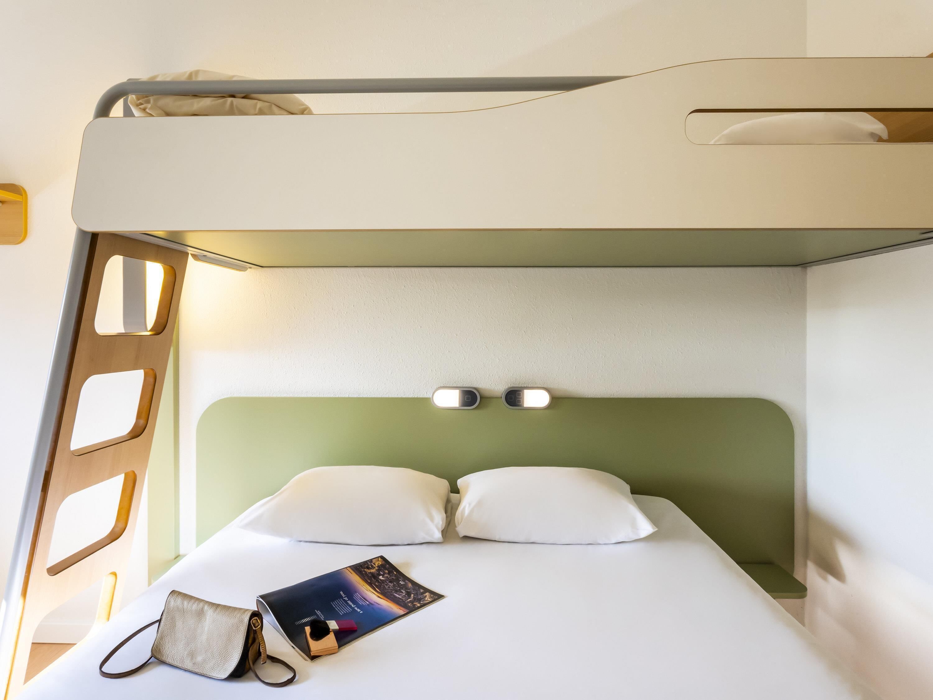 A bunk bed with a headboard, a bedside table with a book and a bag, and a wall-mounted light fixture.