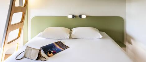 A bunk bed with a headboard, a bedside table with a book and a bag, and a wall-mounted light fixture.