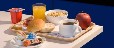 A breakfast tray with a croissant, apple, coffee cup, orange juice, yogurt, and cereal.