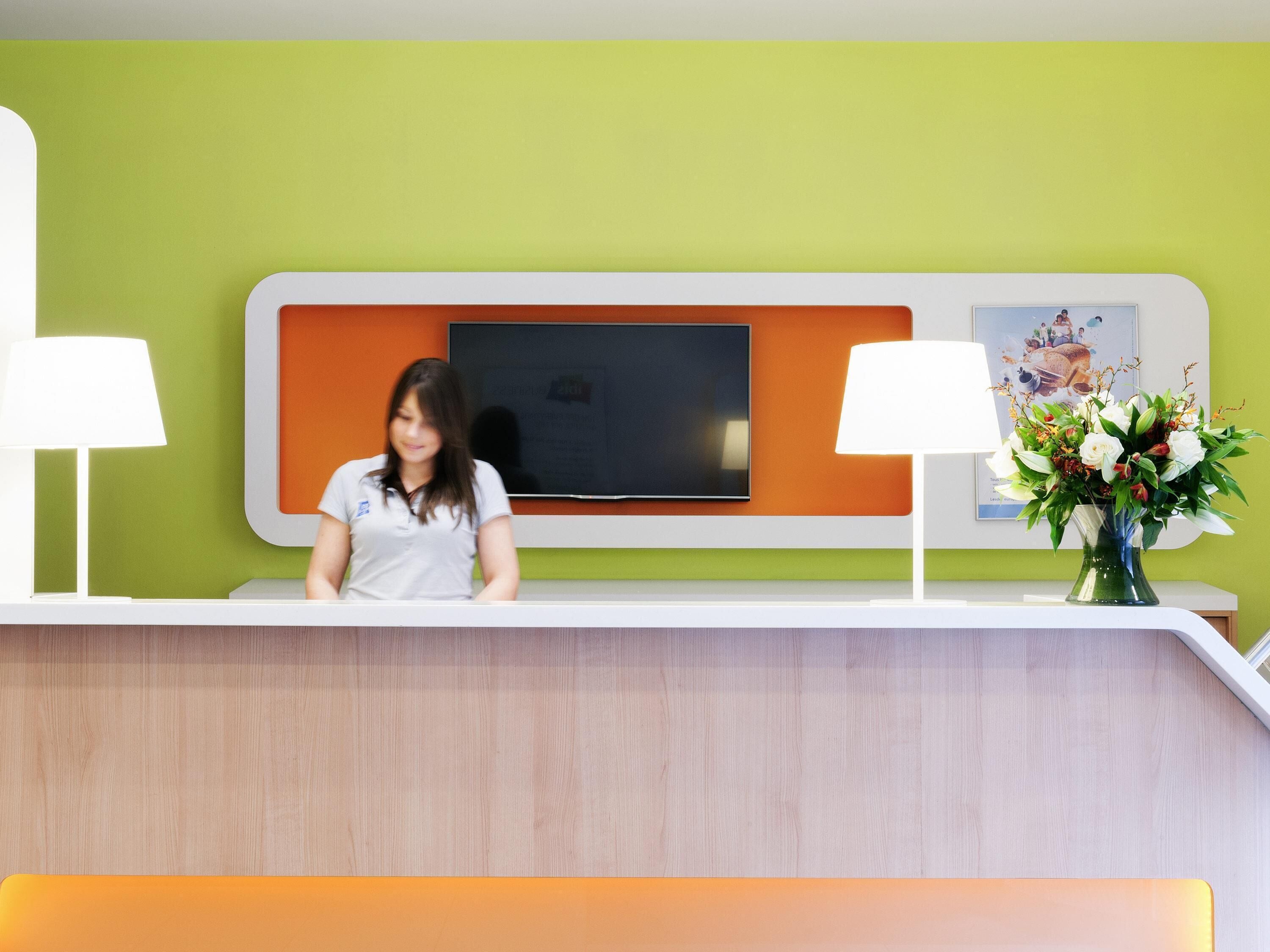 A reception desk with a flat-screen TV, two lamps, and a vase of flowers.