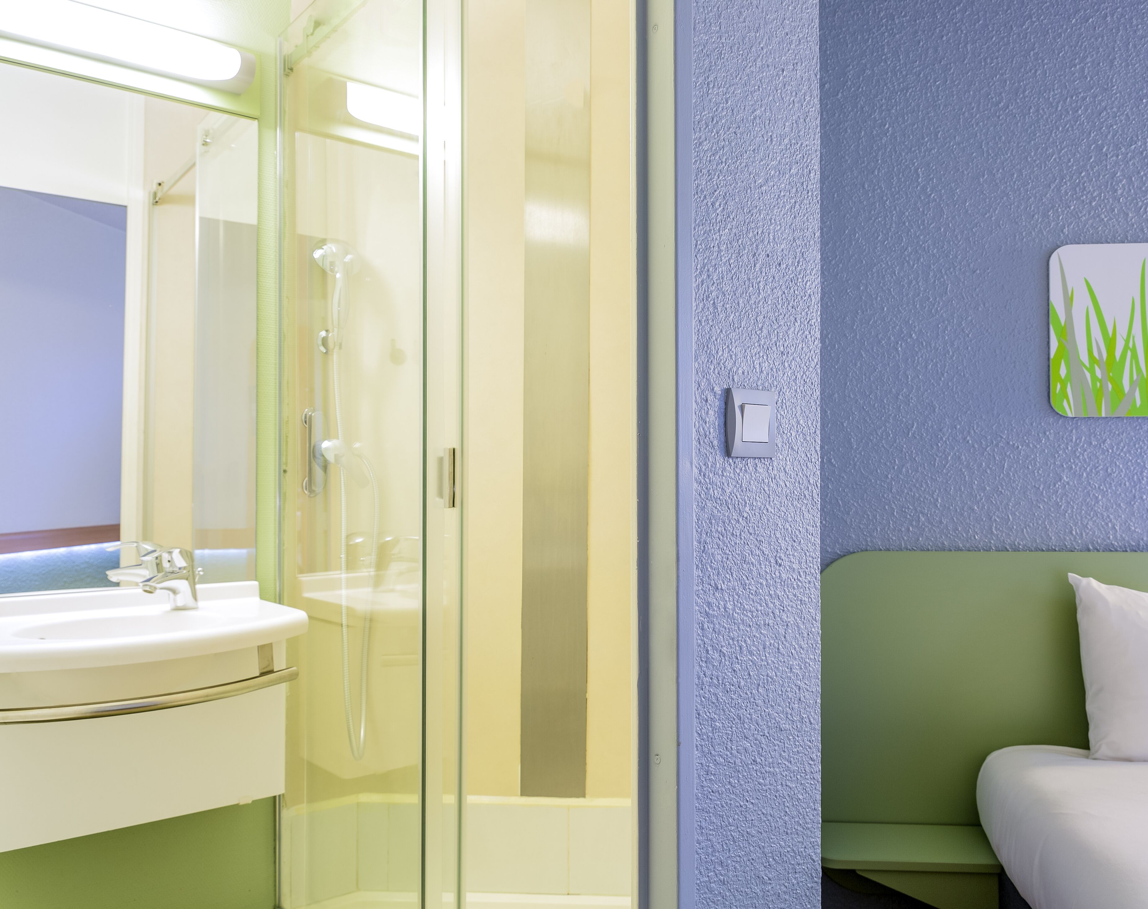Un baño moderno con ducha envuelta en vidrio, un lavabo blanco y un sofá verde.