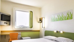 A hotel room with a bed, a desk, a chair, a television, and a window with curtains.