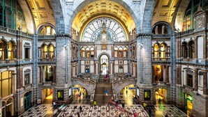 A spacious lobby with a high ceiling and large windows, featuring a central staircase and multiple levels.
