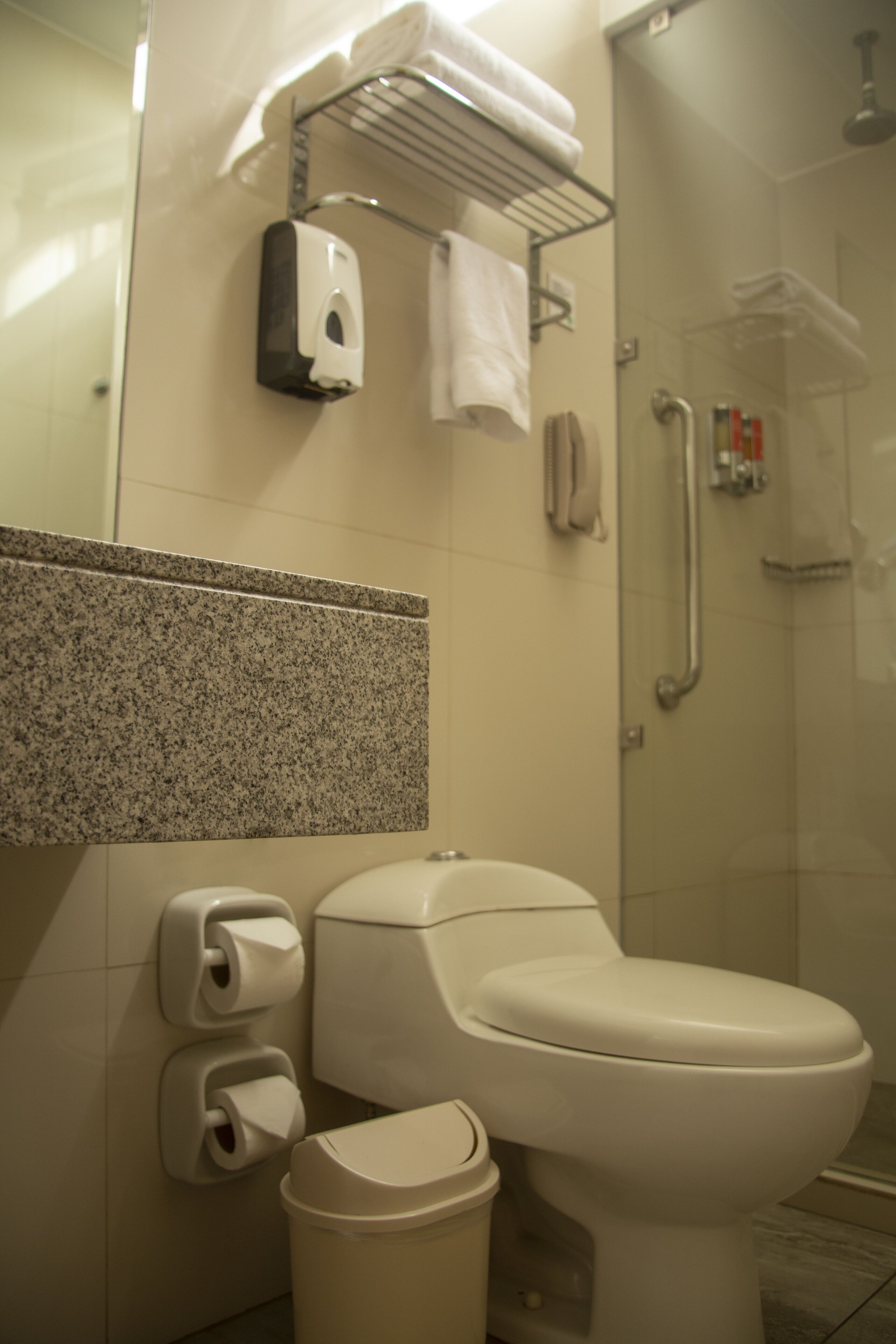 Een badkamer met toilet, handdroger, papieren handdoekdispenser en een douchecabine met glazen wanden.
