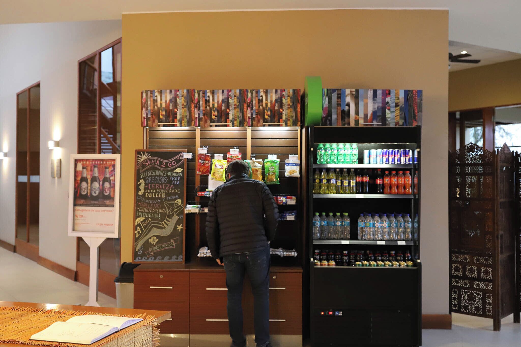 Un hombre de pie frente a una máquina expendedora llena de refrigerios y bebidas.