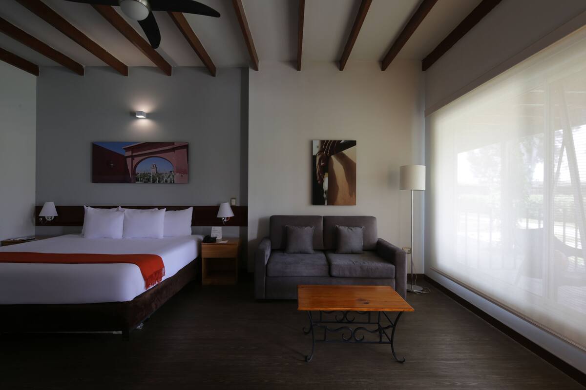 Una habitación de hotel con una cama, un sofá, una mesita de café y un ventanal grande.
