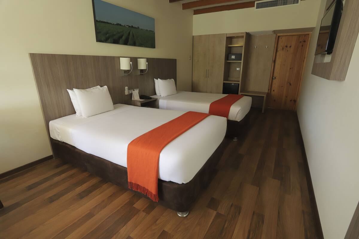 Una habitación de hotel con dos camas, suelo de madera, un cuadro en la pared y un armario.