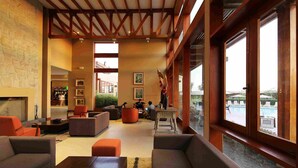 A spacious lobby with a stone wall, wooden beams, and large windows overlooking a pool area. - Casa Andina Standard Chincha (Sunampe)
