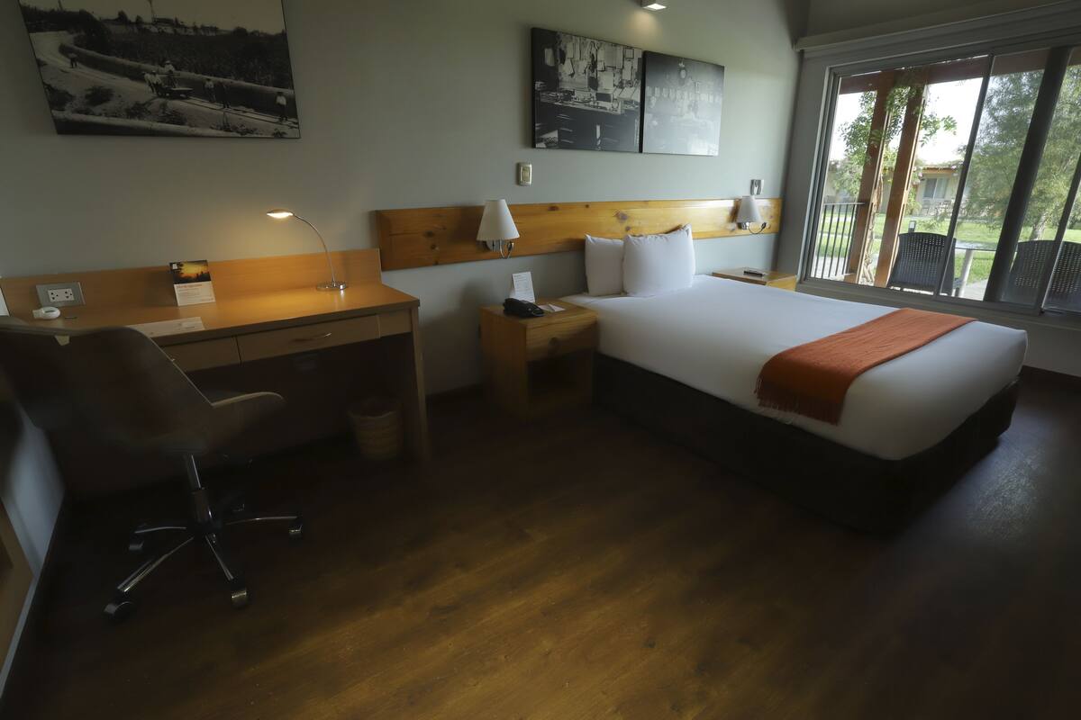 Habitación de hotel con cama, escritorio, silla, mesita de noche y vistas al exterior.