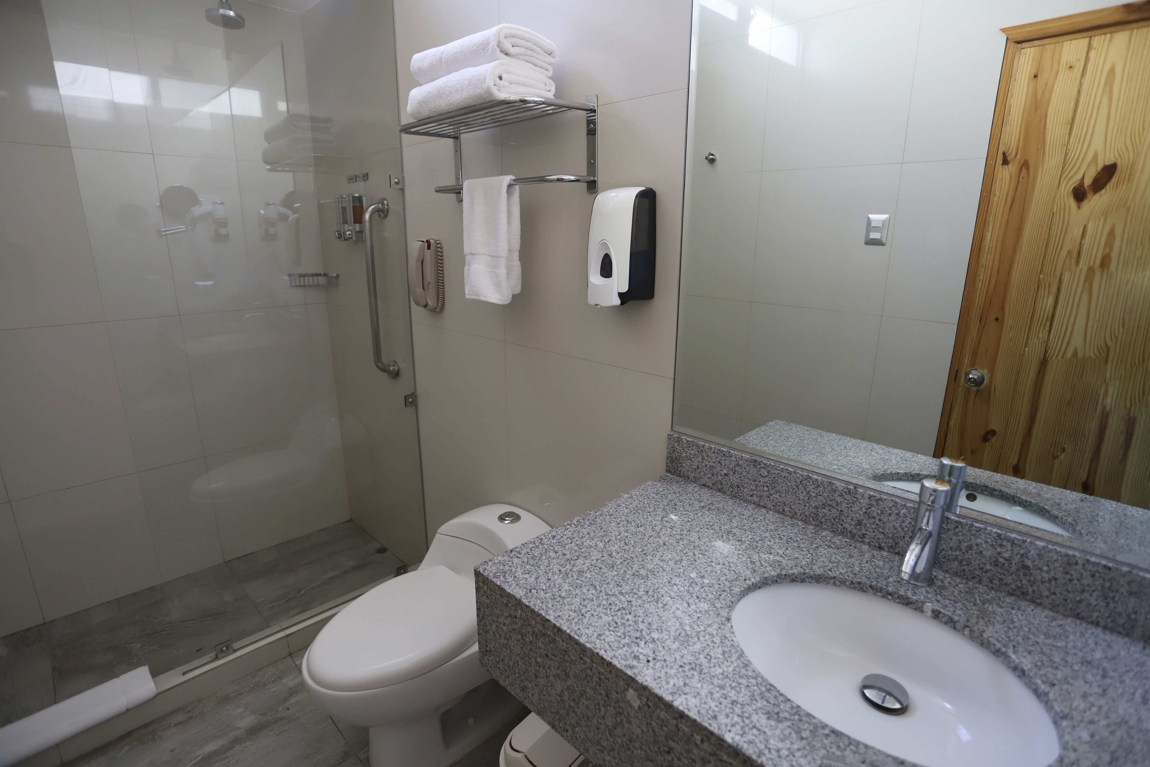 Un baño con ducha, inodoro, lavamanos y puerta de madera.