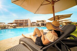 A poolside lounge area with wicker chairs and umbrellas, a pool, and modern buildings in the background. - Casa Andina Standard Chincha (Sunampe)