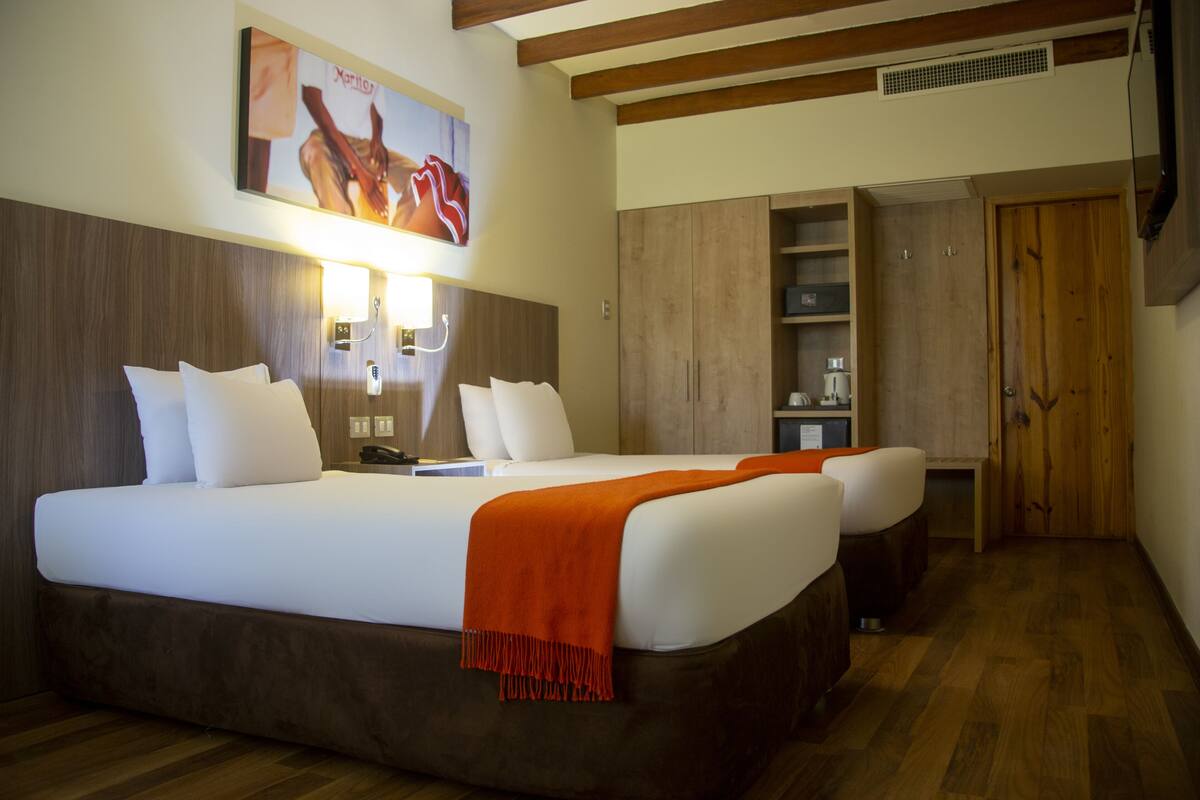 Una habitación de hotel con una cama grande, mesitas de noche, un armario y un cuadro en la pared.