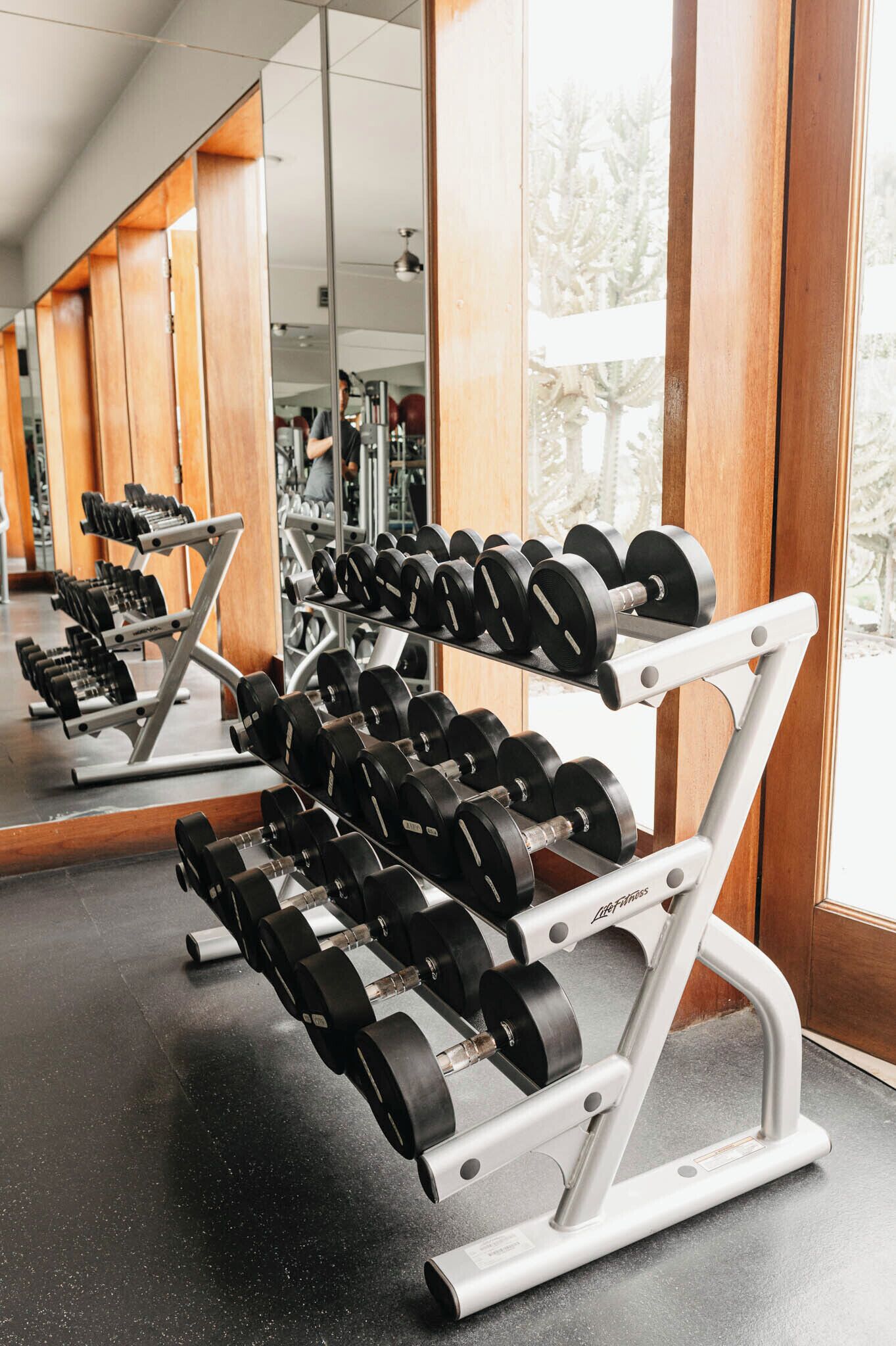 Un gimnasio con equipo de levantamiento de pesas, amplias ventanas y suelo pulido.