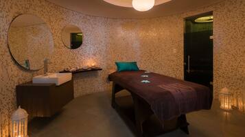 Une salle de spa moderne équipée d’un grand miroir, d’une table de massage, d’un lavabo et d’une petite étagère avec des bougies.
