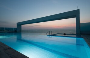 Ein Indoor-Pool mit moderner Architektur, der sich durch eine große, überhängende Struktur und einen klaren Blick auf den Sonnenuntergang im Hintergrund auszeichnet.
