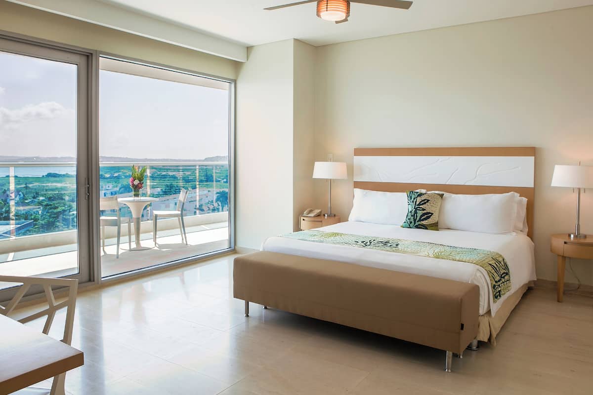 Una camera d'albergo con un letto, comodini, una ventola a soffitto e un balcone con tavolo e sedie.