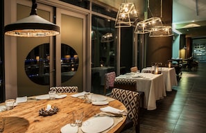 Ein Restaurant mit runden Tischen, gemusterten Stühlen und Pendelleuchten.