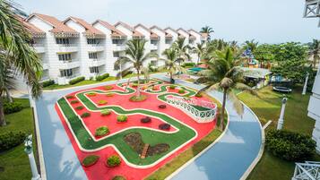 A hotel with a courtyard featuring a geometric garden design, palm trees, and a white building with red-tiled roofs.