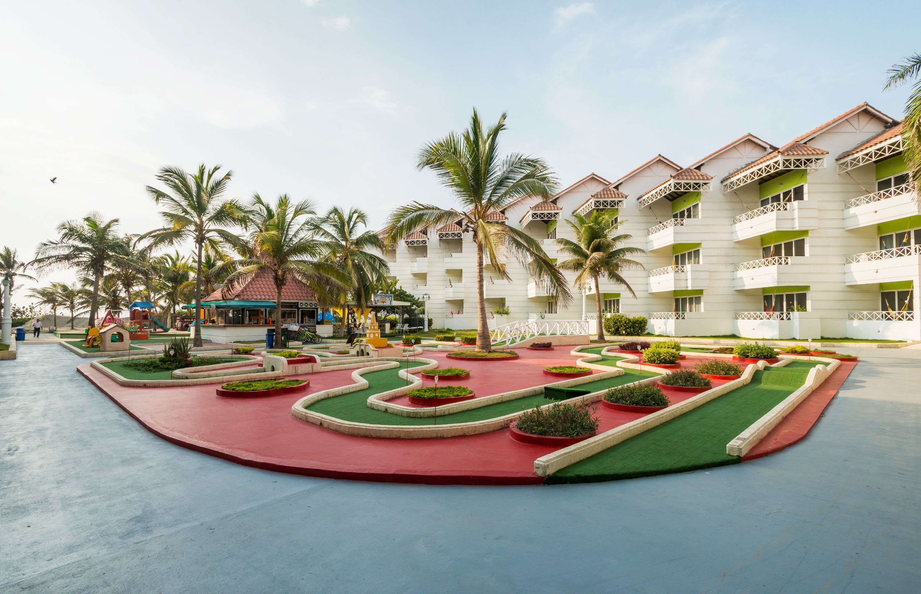 A hotel courtyard with palm trees, a children's play area, and a red and green landscaped garden.
