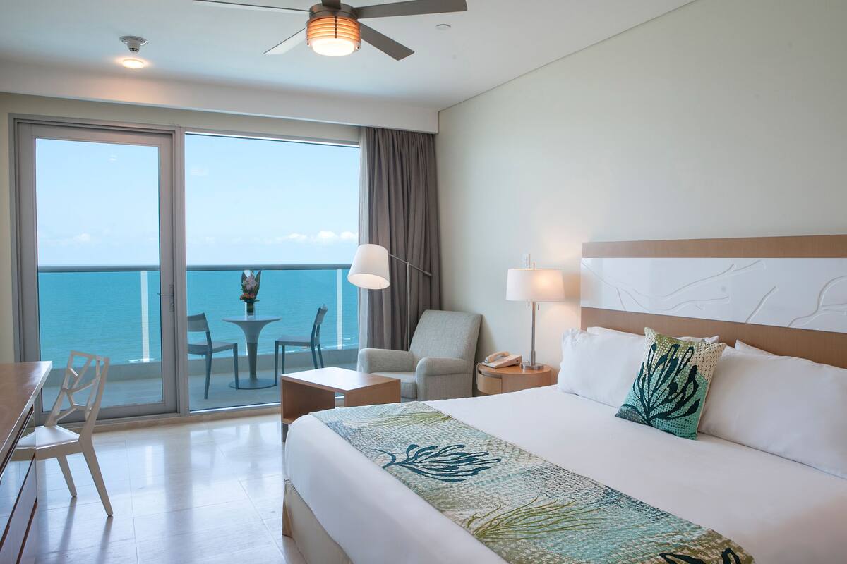Una camera d'albergo con un letto grande, una scrivania, una sedia, un tavolo e vista sull'oceano.