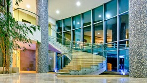 A modern hotel lobby with a glass staircase, large windows, and decorative pillars.