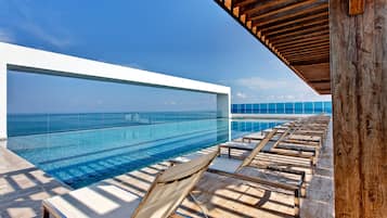 Zona de piscina con sillones de descanso y vista al océano.