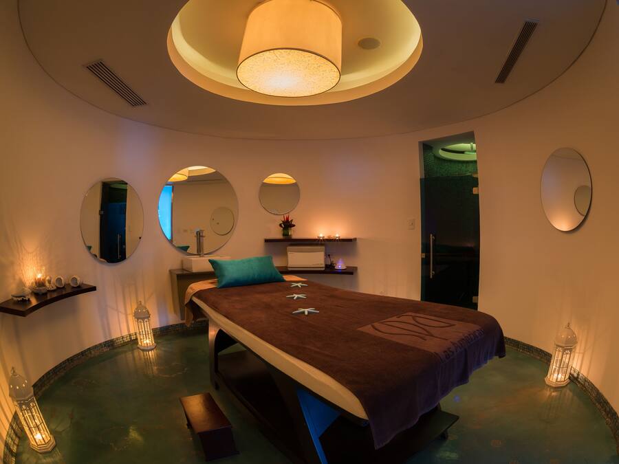 A spa room with a bed, mirrors, a sink, and a massage table.