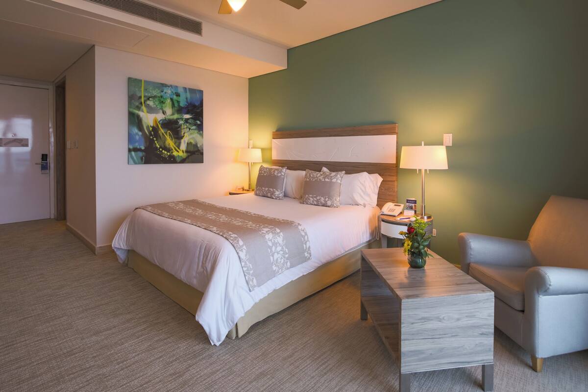 Una camera d'albergo con un letto, due lampade da comodino, un comodino, una sedia, un tavolino e una ventola a soffitto.