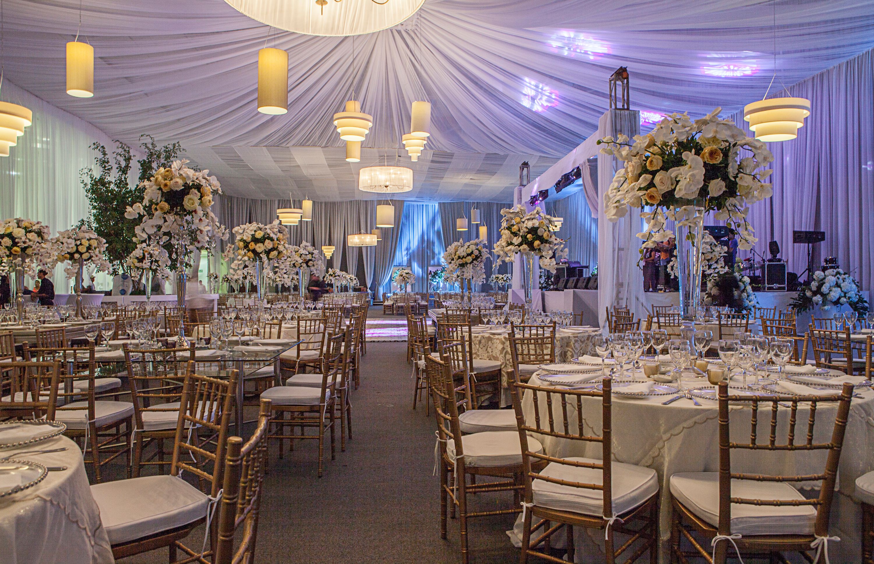 A banquet hall with round tables, wooden chairs, and floral centerpieces.