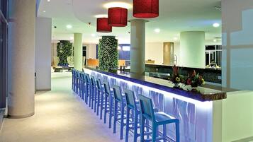 A modern hotel lobby with a long reception counter, blue chairs, and red pendant lights.