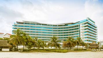 A multi-story hotel with a curved facade, palm trees, and a beach in the foreground.