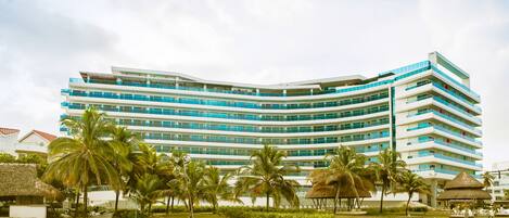 Un hôtel à plusieurs étages, doté d’une façade incurvée, de palmiers et d’une plage en premier plan.