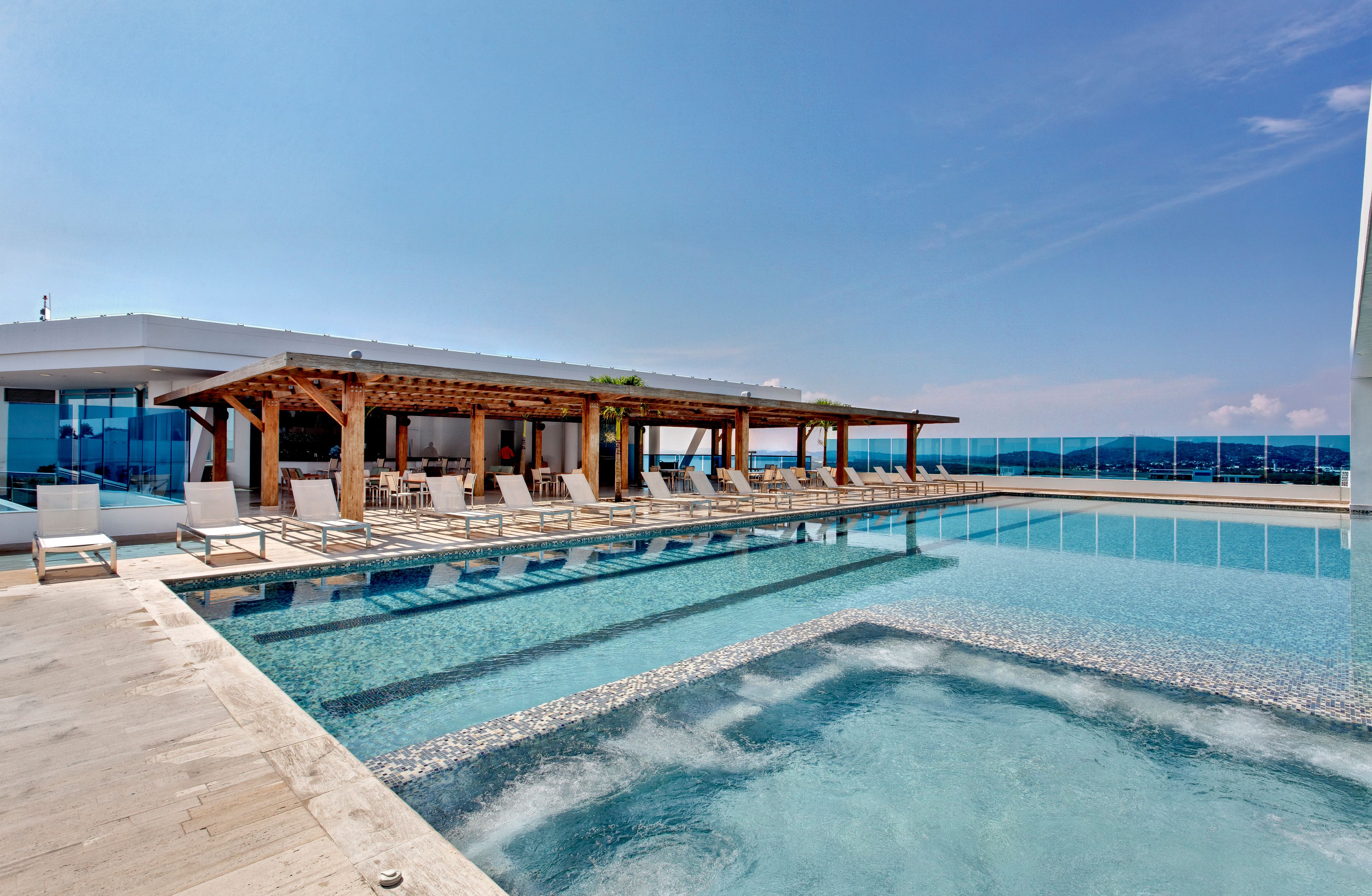 Une piscine à débordement située sur le toit, avec des chaises longues et un espace salon abrité.