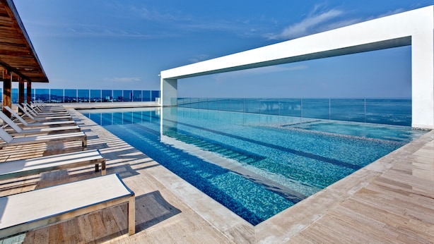 A modern infinity pool with clear blue water, lounge chairs, and a view of the ocean.