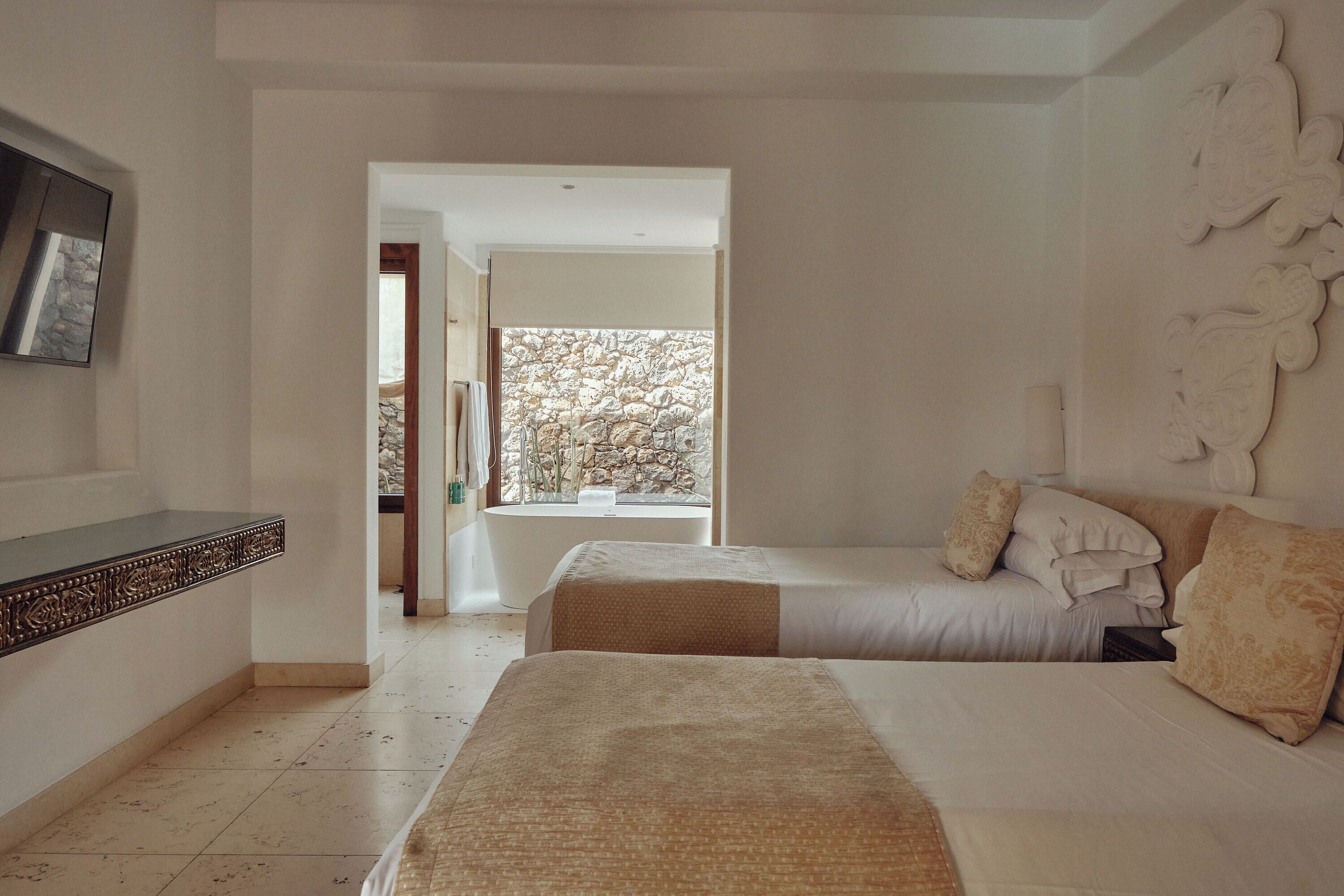 Un dormitorio con dos camas, una bañera y un ventanal con vistas a árboles.