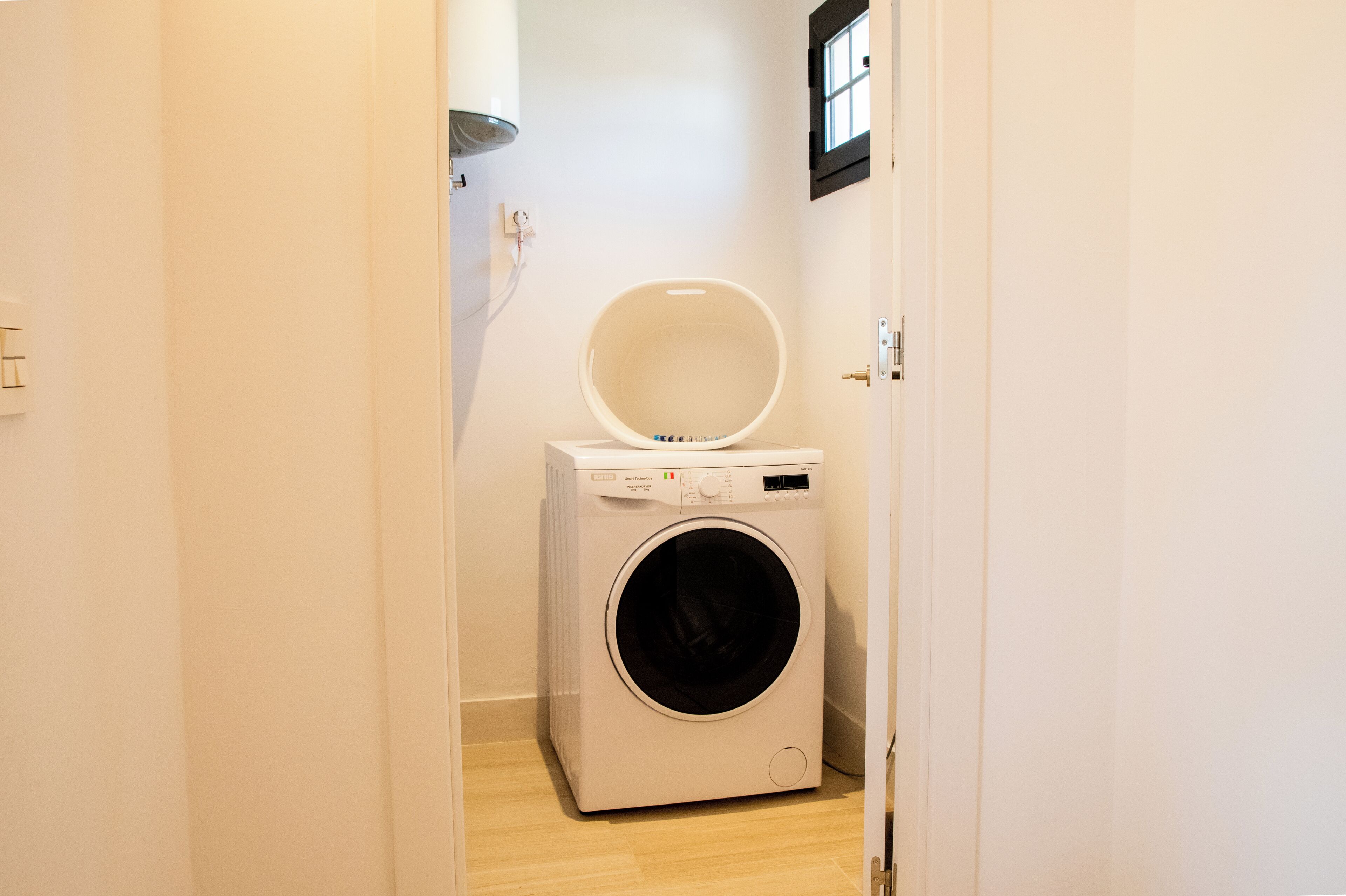 A compact, white laundry room with a front-loading washing machine and a small window above the door.