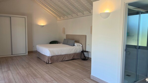 A bedroom with a bed, a chair, a bedside table, and a glass shower enclosure. - Hotel Villas Alondra (TÃas)