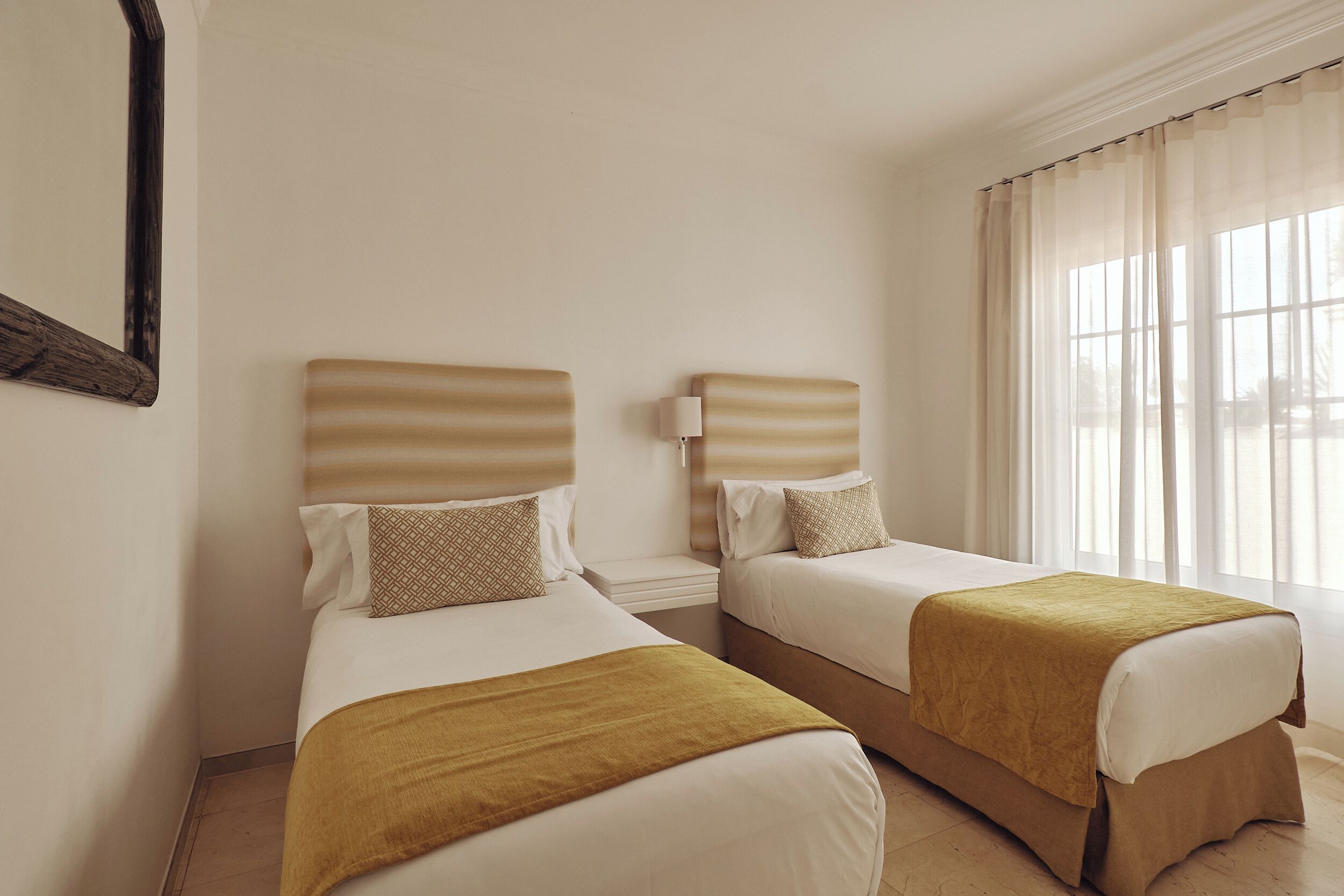 A hotel room with two beds, each with a headboard and a bedside table.
