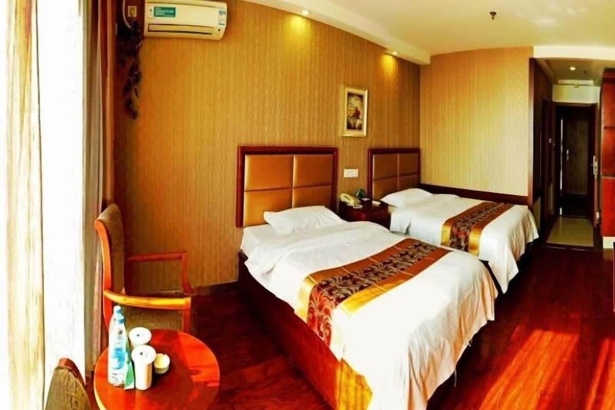 Habitación de hotel con dos camas, piso de madera, una mesita con artículos de aseo y un equipo de aire acondicionado.