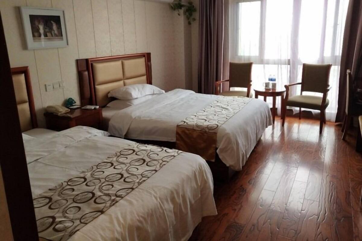 Habitación de hotel con dos camas, una mesita de noche, una silla y un ventanal con cortinas.