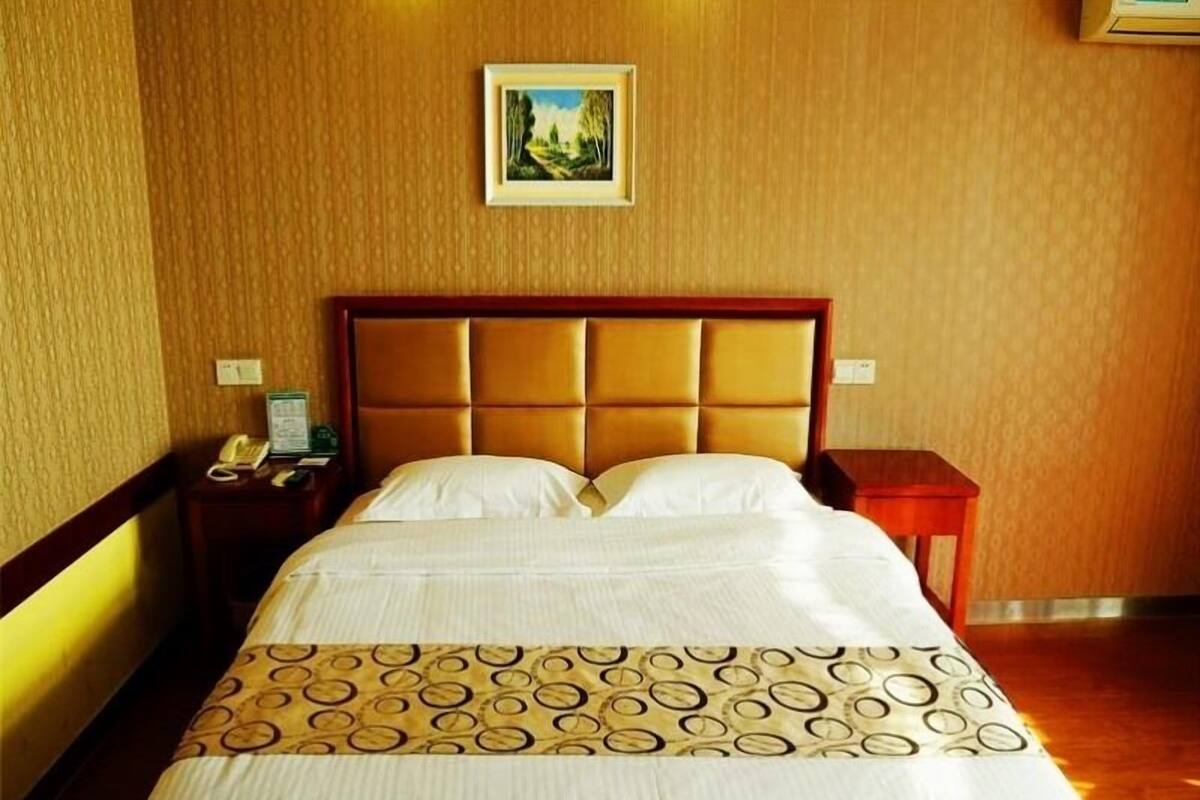 Un cuarto de hotel con una cama grande, un cabecero de madera, una mesita de noche con una lámpara y un cuadro en la pared.