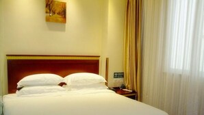 A hotel room with a large bed, a wooden headboard, a nightstand with a phone, and a painting on the wall. - Greentree Jiangsu Yizheng East Zhenzhou (Yangzhou)